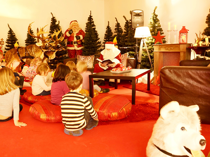 Weihnachtsmann liest Kindern Geschichten vor in Kulisse mit Rentieren